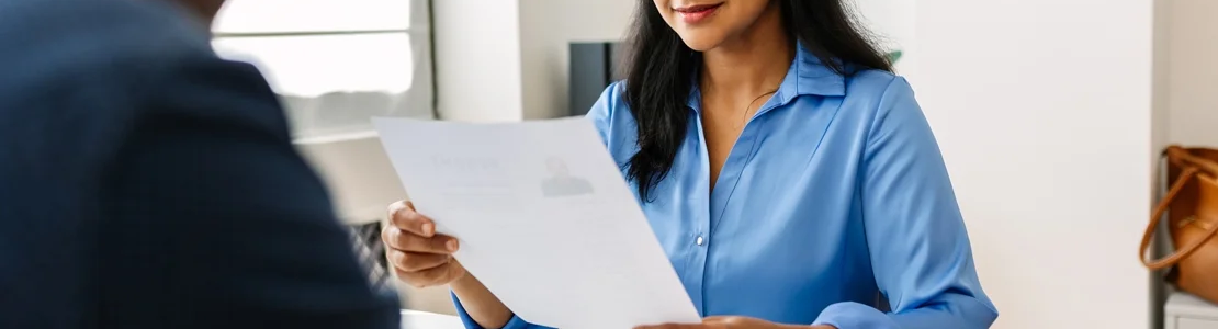 A woman sitting across from a man in a suit, looking over a resume.