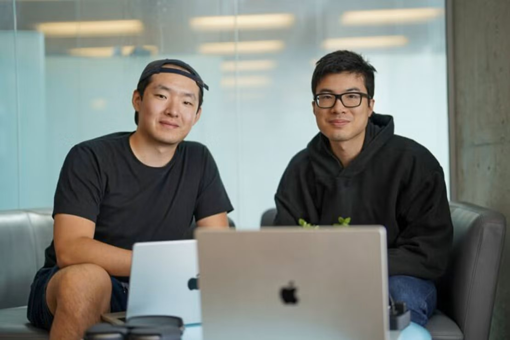 Two U of T alumni sit together on a couch, with their laptops open in front of them. They are both smiling at the camera.